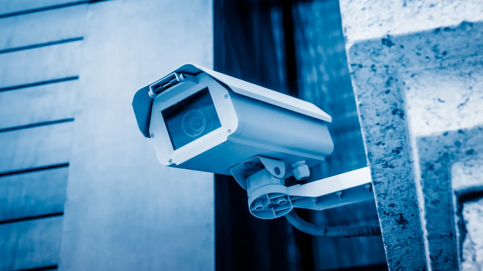 Modern CCTV security camera mounted on a building corner, blue-tone night surveillance