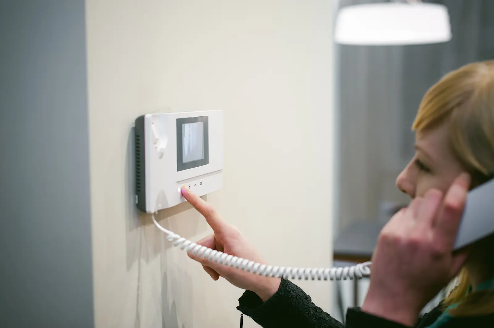 Person using a wall-mounted video intercom system to verify a visitor at the door