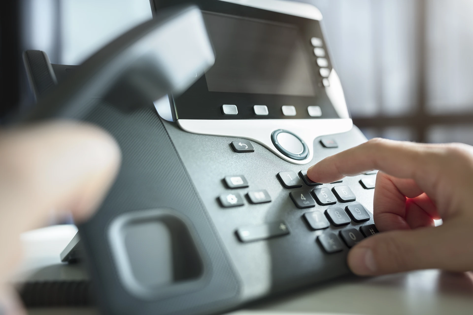 Modern IP desk phone with hand pressing keypad — business PABX telephony